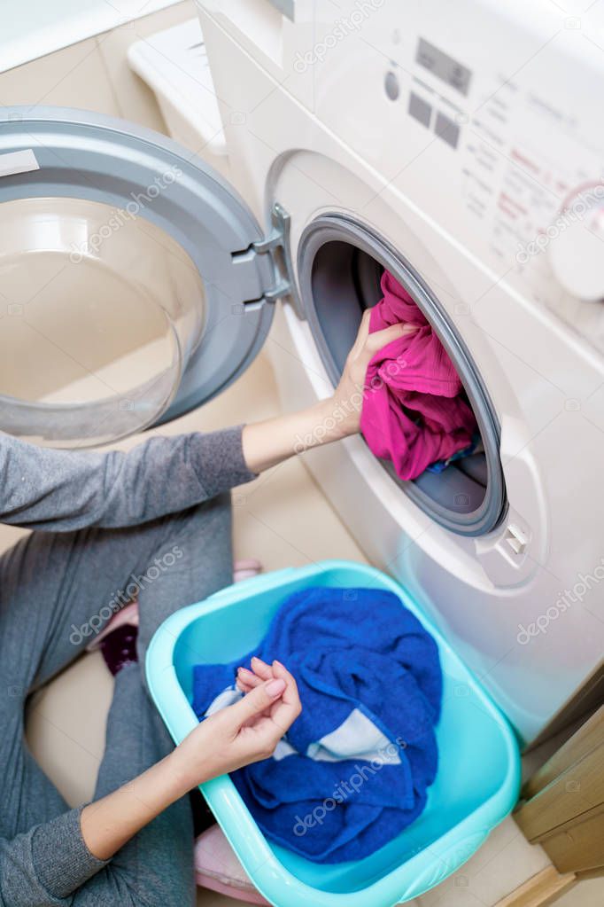 Photo from above of female hands putting dirty pink clothes in washing machine .