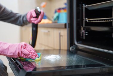 Pembe eldiven sünger ve fırın yıkama sprey ile kadının görüntüsünü eller.