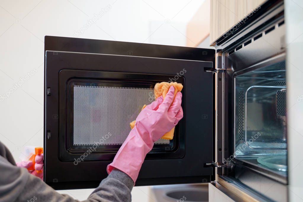 Photo of woman hands in rubber gloves washing microwave