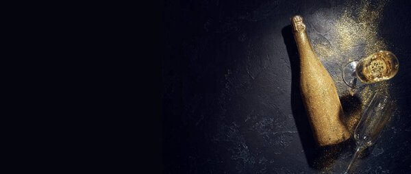 Romantic photo of golden champagne bottle, two wine glasses on black background