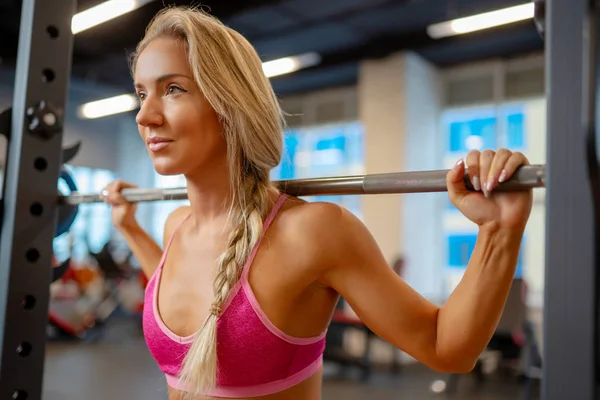 Портрет молодої спортивної блондинки, що стоїть з барбелом на плечах у спортзалі . — стокове фото