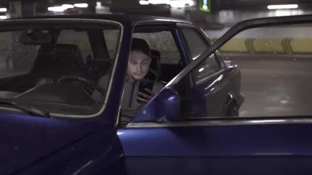Młody człowiek z inteligentny telefon siedzi w samochodzie i na czacie. — Wideo stockowe