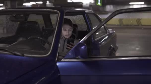 Jovem com telefone inteligente sentado em seu carro e conversando . — Vídeo de Stock