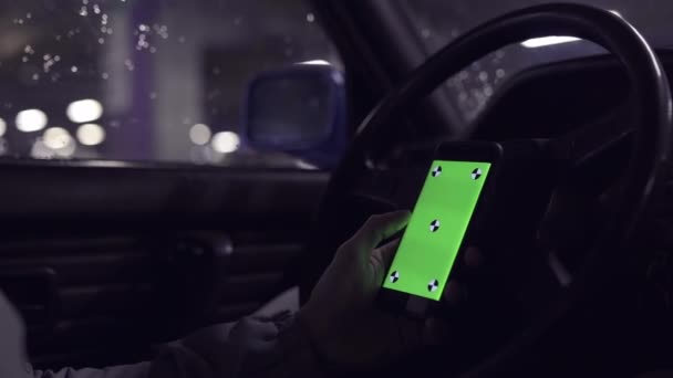 El hombre se sienta en el coche viejo y sostiene el teléfono inteligente con pantalla verde. Clave de croma . . — Vídeo de stock