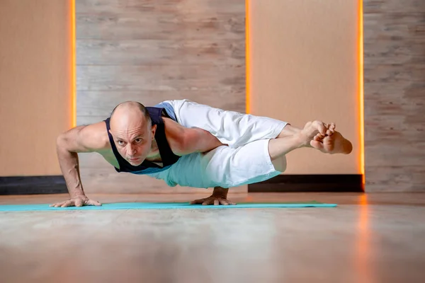 Atleta hombre practica yoga mientras de pie en las manos en la estera azul  . — Foto de Stock