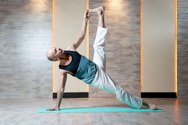 Atletisk man på arm och ben med handen upp gör yoga på blå matta. — Stockfoto