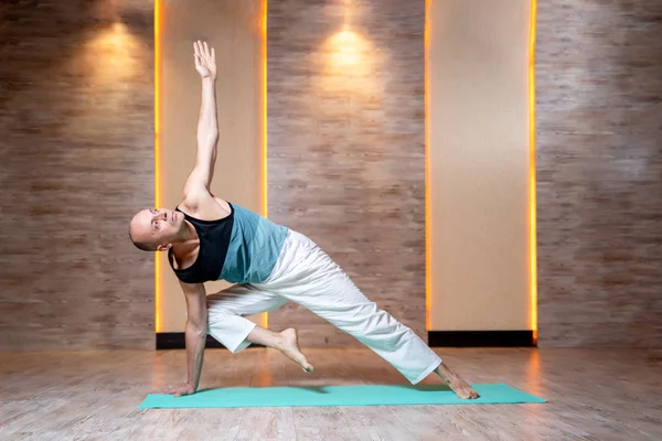 Man praktiserar yoga medan stående på ena armen och benet på blå matta. — Stockfoto