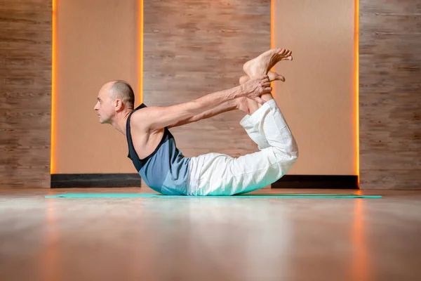 Adult man practicing yoga lying on his stomach on blue mat.