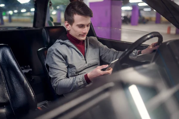 Foto de lado do jovem motorista masculino com telefone nas mãos sentado no carro . — Fotografia de Stock