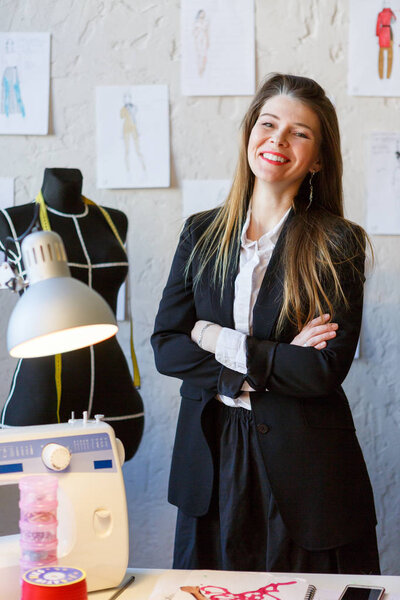 Photo of happy seamstress woman with arms crossed at waist standing next to mannequin.