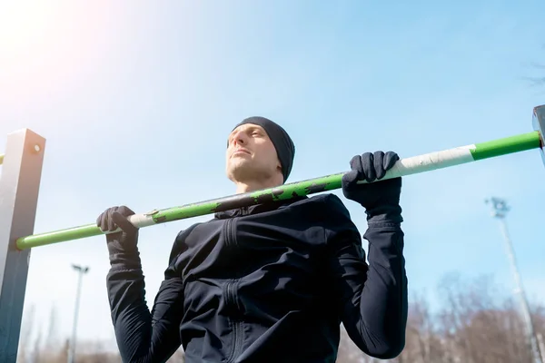 Foto do jovem atleta puxando para cima na barra horizontal verde — Fotografia de Stock