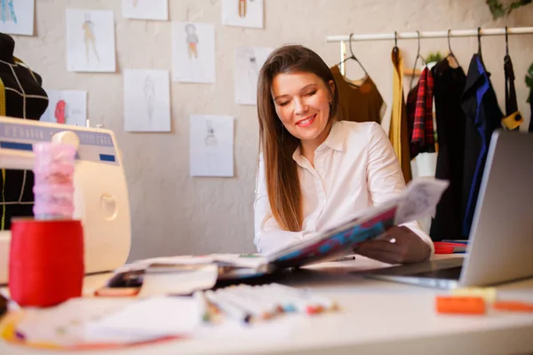 Фото щасливої жінки-виробника, що сидить за столом зі швейною машиною та каталогом — стокове фото