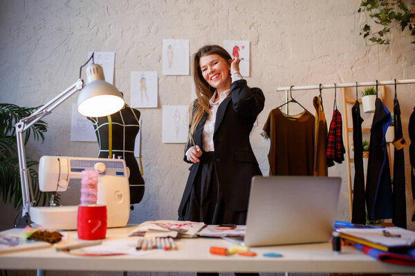 Photo of female dressmaker standing next to mannequin, hanging dresses.