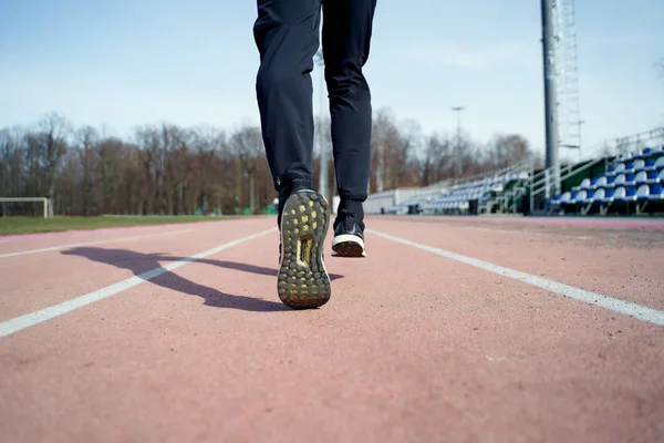 Photo from back of legs of athlete running through stadium — Stock Photo, Image