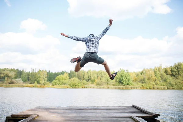 Foto van de achterkant van Jumping man op houten brug door rivier — Stockfoto