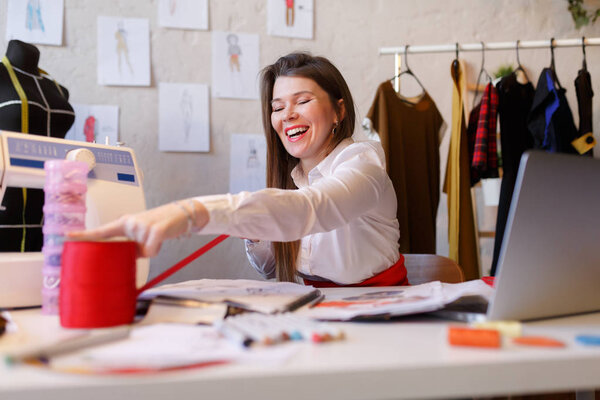 Photo of female dressmaker unwinding red ribbon sitting at table