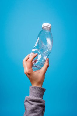 Mavi arka plana karşı elinde plastik şişe.