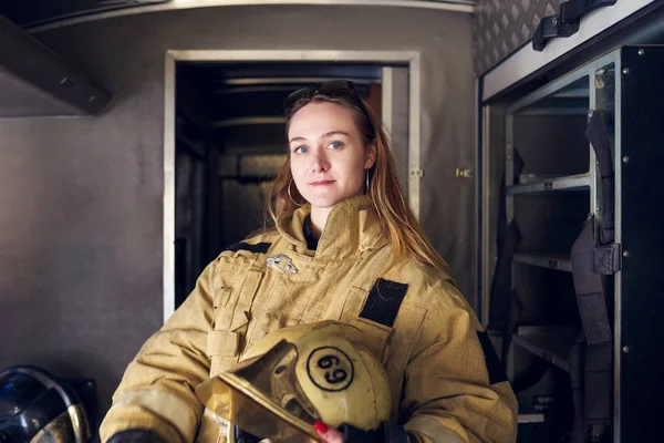 Foto de mulher bombeira com capacete nas mãos em pé no caminhão de bombeiros — Fotografia de Stock