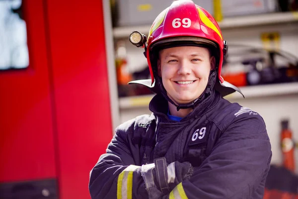 Foto eines glücklichen männlichen Feuerwehrmannes mit Helm auf dem Hintergrund eines Feuerwehrfahrzeugs — Stockfoto