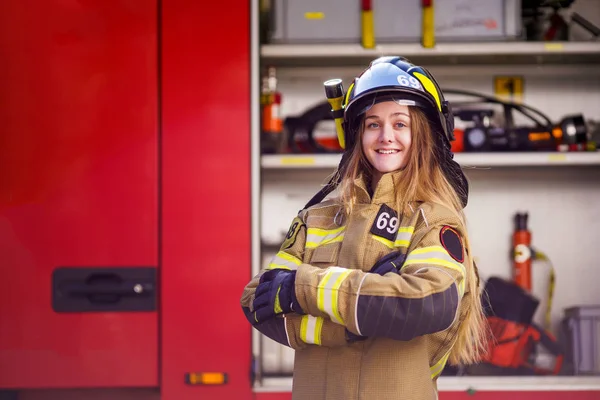 Foto de mujer bombero en casco con los brazos cruzados de pie cerca de camión de bomberos — Foto de Stock