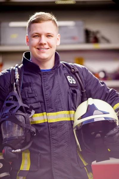 Imagen de feliz bombero masculino con casco en las manos contra el fondo del camión de bomberos — Foto de Stock