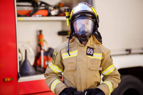 Imagem de mulher bombeira no capacete e máscara de pé perto do caminhão de bombeiros — Fotografia de Stock