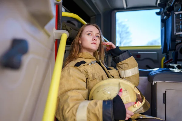 Zdjęcie kobiety strażak z hełmem w rękach siedzi w Fire Truck — Zdjęcie stockowe