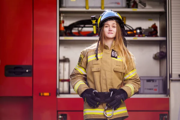 Bild eines blonden Feuerwehrmannes mit Helm, der in der Nähe eines Feuerwehrfahrzeugs am Feuerwehrhaus steht — Stockfoto