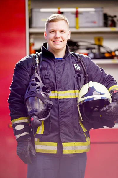 Foto de hombre feliz bombero con casco en las manos contra el fondo de camión de bomberos —  Fotos de Stock