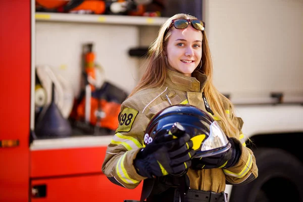 Image of woman firefighter with helmet in her hands standing near fire truck