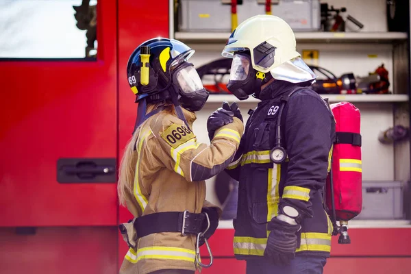 Imagen de bomberos mujeres y hombres en casco y máscara mirándose y haciendo apretón de manos cerca de camión de bomberos — Foto de Stock