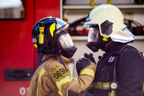 Fotos de bomberos mujeres y hombres en casco y máscara mirándose y haciendo apretón de manos cerca de camión de bomberos — Foto de Stock