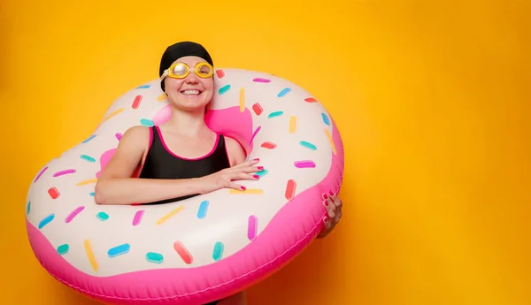 Photo of happy girl in swimming goggles, swimsuit with donut life buoy on empty orange background — Stock Photo, Image