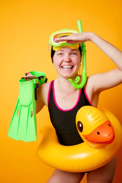 Foto de mulher feliz com barbatanas nas mãos, máscara de natação e com salva-vidas em fundo laranja vazio — Fotografia de Stock