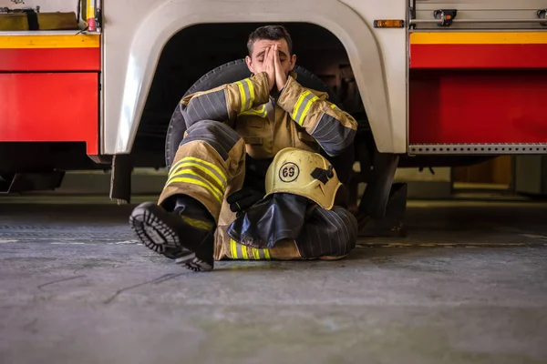 Картина втомленого пожежника, що сидить на підлозі біля червоної пожежної машини — стокове фото