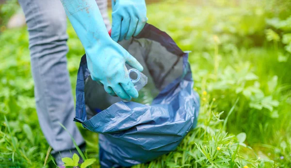 Imagen de la mujer en guantes de goma recogiendo la botella de plástico sucio en el bolso en el césped verde — Foto de Stock