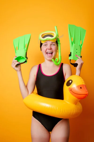 Foto de mujer sonriente con aletas en las manos, máscara de natación y con salvavidas sobre fondo naranja vacío — Foto de Stock