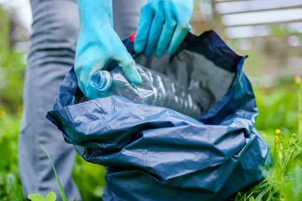 Foto de niña en guantes de goma recogiendo botella de plástico sucio en el bolso en el césped verde — Foto de Stock