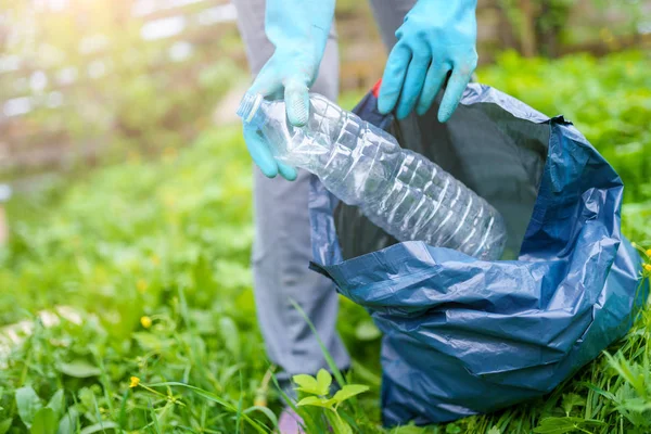 Фото человека в резиновых перчатках, собирающего грязную пластиковую бутылку в мешок на зеленой лужайке — стоковое фото