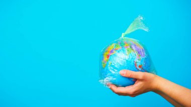 Kadın, mavi arka planda dünya gezegeninin plastik torbasıyla el ele tutuşuyor. Plastik kirliliği kavramı.