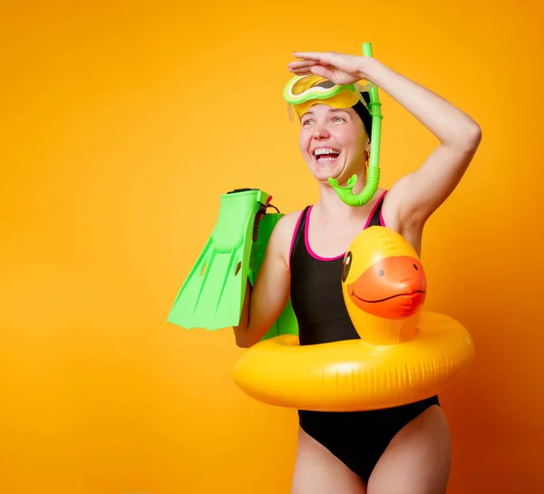 Foto de chica feliz con aletas en las manos, máscara de natación y con salvavidas sobre fondo naranja vacío — Foto de Stock