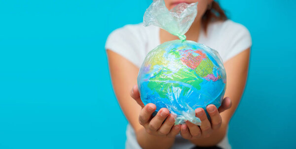 Woman holds in hands plastic bag with planet earth at blue background. The concept of plastic pollution.