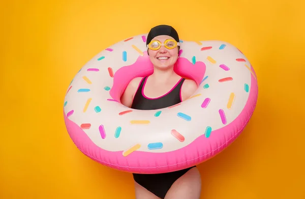 Picture of happy woman in swimming goggles, swimsuit with donut life buoy on empty orange background — Stock Photo, Image