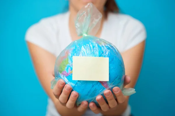 Kadın elinde boş yapıştırmalı plastik torba ve mavi arka planda dünya gezegeni.. — Stok fotoğraf