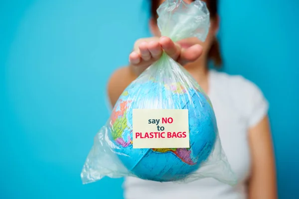 Mulher segura em mãos saco de plástico com texto adesivo dizer NÃO a BAGAS PLÁSTICAS e planeta terra em fundo azul. O conceito de poluição plástica . — Fotografia de Stock