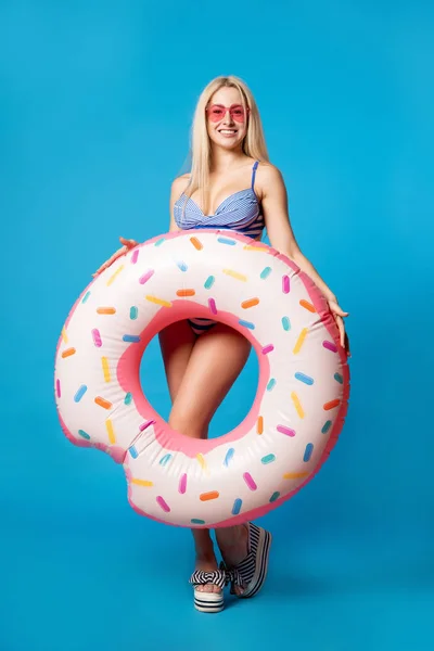 Foto de cuerpo entero de mujer joven en traje de baño con rosquilla inflable sobre fondo azul vacío — Foto de Stock