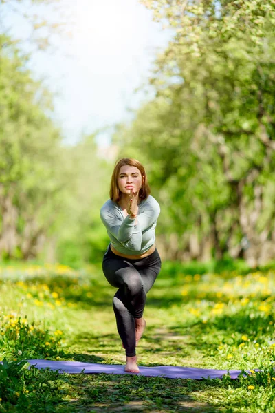 Foto de una mujer haciendo yoga de pie sobre una alfombra azul en el bosque —  Fotos de Stock