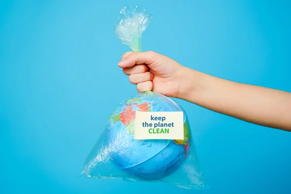 Vrouw houdt in handen plastic zak en planeet aarde met tekst sticker- houd Planet Clean op blauwe achtergrond. Het begrip plasticvervuiling. — Stockfoto