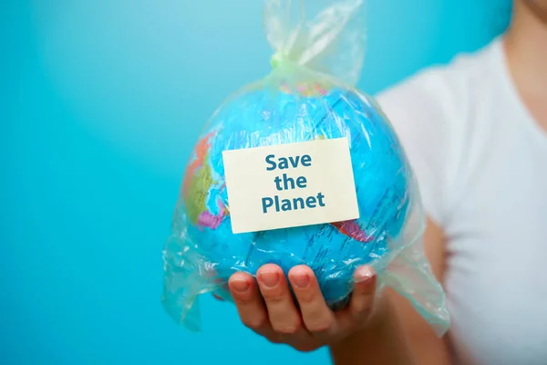 Mulher segura em mãos saco de plástico com texto adesivo Salve o PLANET e planeta terra em fundo azul. O conceito de poluição plástica . — Fotografia de Stock