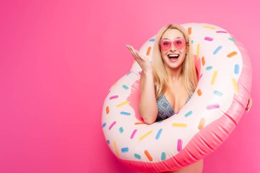 Boş pembe arka plan üzerinde yüzmek için şişme donut ile mayo güneş gözlüğü kız Görüntü. Elle yana gösterir